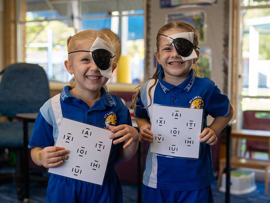 2 young girls smiling gleefully with eye patches on, holding sheets used for vision screening