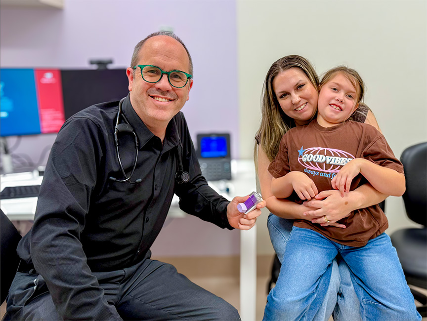 Three people in a room. One of them is sitting on a persons lap. 