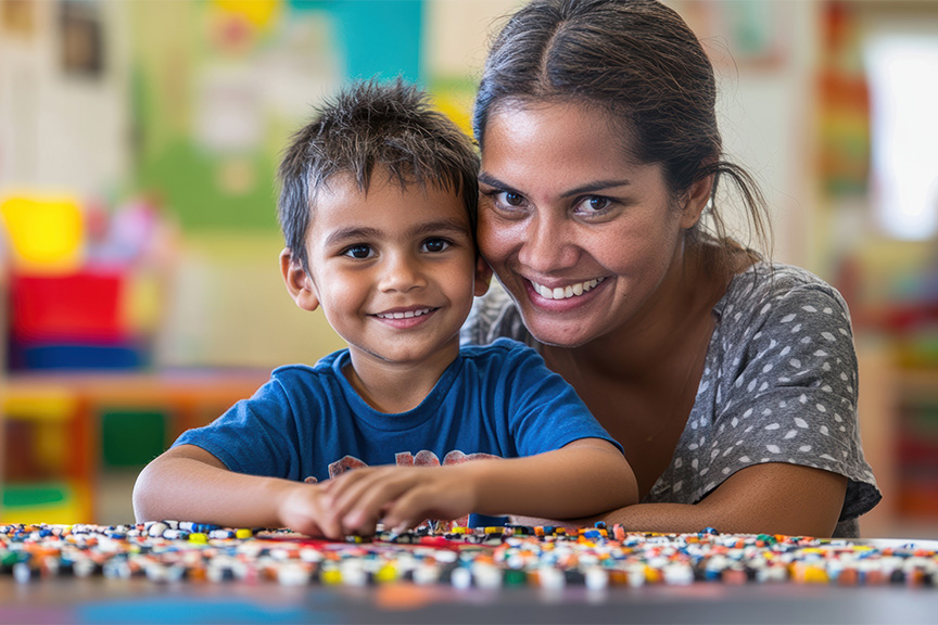 A mother and her young son, both with dark hair, sitting at a table looking at the camera smiling