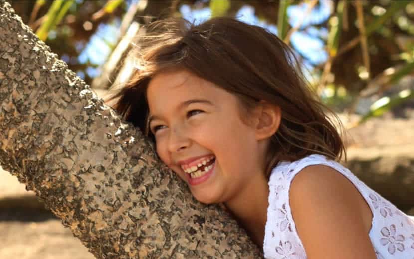 A young girl is smiling and leaning against a tree branch.