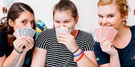 3 young people playing cards in bed and smiling