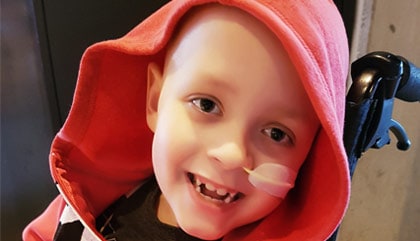 A young boy with a red hoodie is smiling.