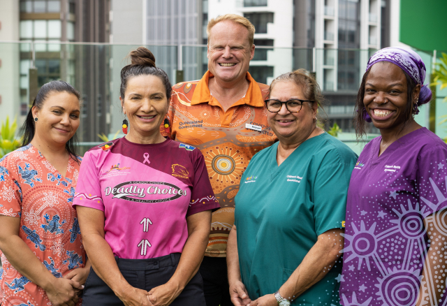A group of diverse healthcare professionals smiling and standing together outdoors, wearing colorful uniforms with Aboriginal and Torres Strait Islander designs