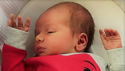 A newborn baby lying on their back with their arms raised.